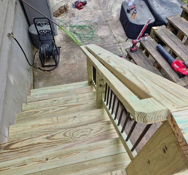 Newly framed pressure-treated deck stairs and railing above a patio
