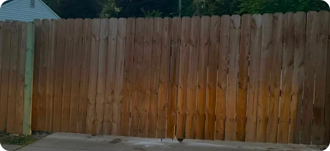 Curving dark stained picket fence running across a lawn